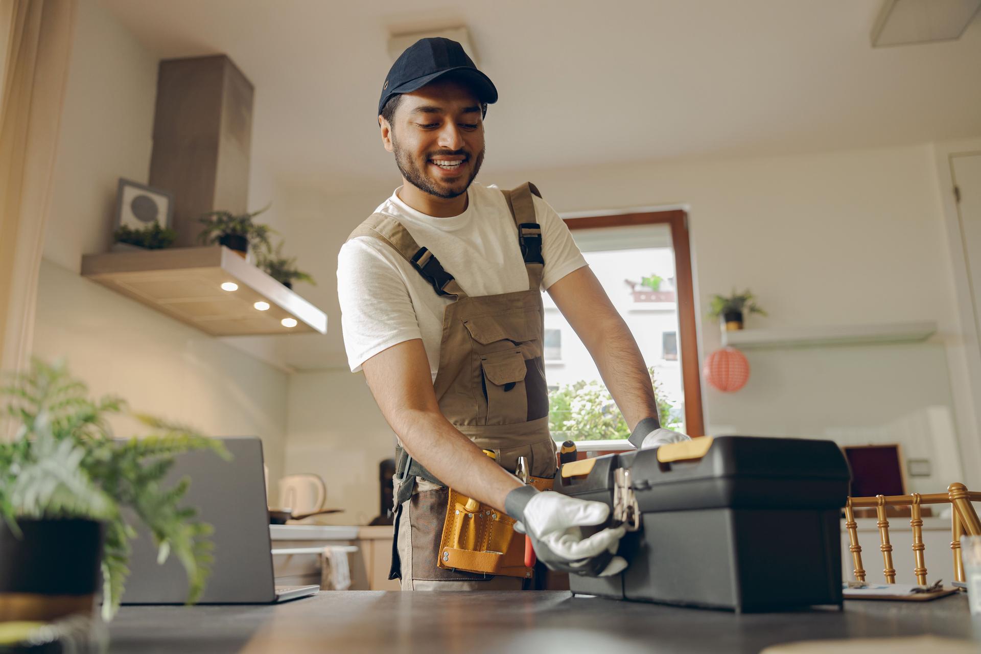 Smiling professional handyman standing on home kitchen and open his tool bag